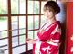 A woman in a red and white kimono standing by a window.