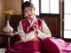 A woman in a pink and white hanbok sitting on the floor.