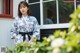 A woman in a blue and white kimono standing in front of a window.