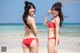 Two women in red bikinis standing on a beach.