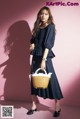 A woman standing in front of a pink wall holding a basket.