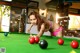 A woman in a bikini playing pool on a green table.