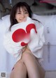 A woman in a white shirt is sitting on a bed.