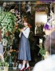 A woman standing in front of a flower shop holding a broom.