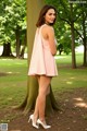 A woman in a pink dress standing next to a tree.