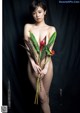 A naked woman holding a bunch of flowers in her hands.